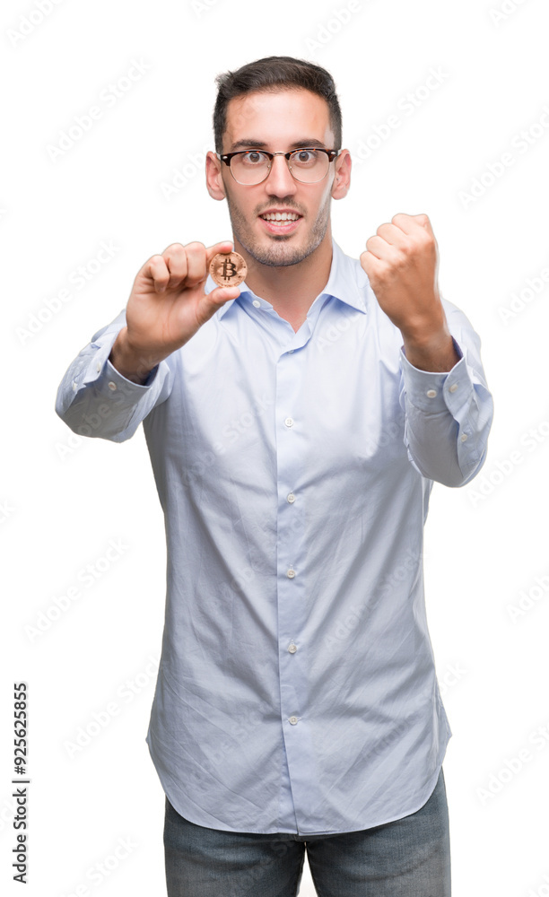 Fototapeta premium Handsome young man holding bitcoin screaming proud and celebrating victory and success very excited, cheering emotion