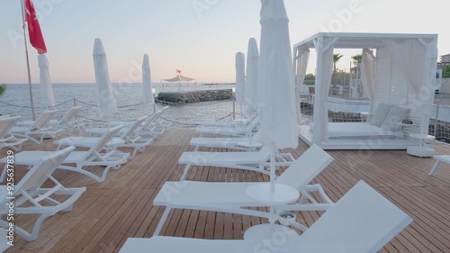 A pristine beachside lounge area featuring white lounge chairs and cabanas, set against the backdrop of calm sea waters, offering a serene and luxurious retreat.