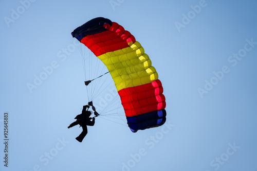 Person flying multi-colored parachute alone for landing in clear blue sky