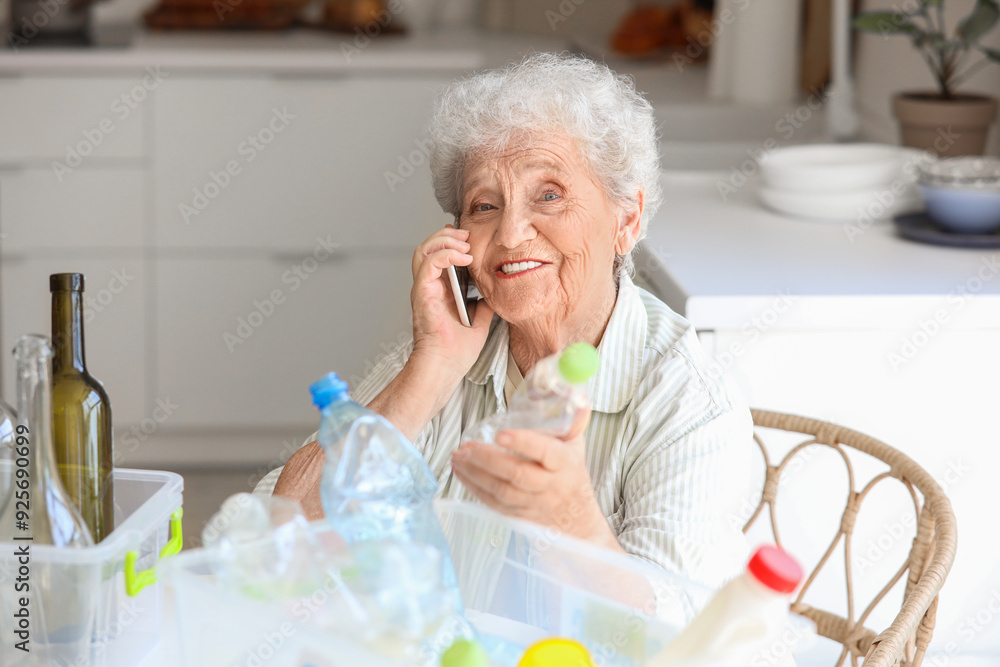 Senior woman with containers of garbage talking by mobile phone at table in kitchen. Waste sorting concept Senior woman with containers of garbage talking by mobile phone at table in kitchen. Waste sorting concept