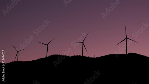 Turkey - November 10 2023: Wind turbines silhouetted against the sunrise sky, with a backdrop of trees, highlighting renewable energy in a serene morning setting.