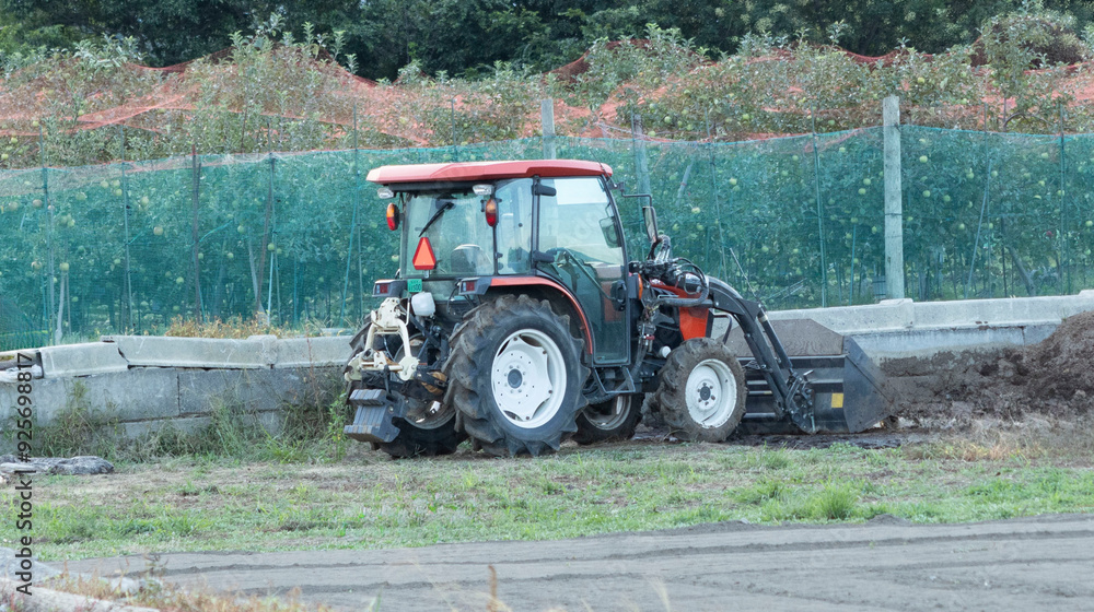 Fototapeta premium Tractor Operating in a Japanese Orchard, Emphasizing the Role of Mechanized Farming Equipment in Maintaining and Protecting Fruit Crops, with Apple Trees Visible in the Background