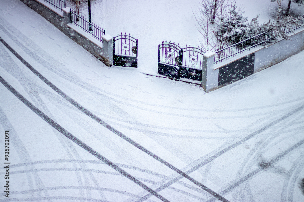 Naklejka premium Snowy road with tire tracks leading to a gate, symbolizing life's paths and new beginnings.