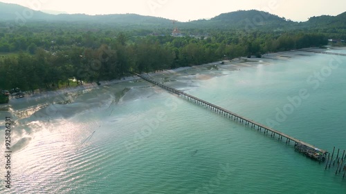 Drone high angle descends to pier stretching from trees along sandy beach shoreline of Koh Rong Island Sihanoukville Cambodia photo