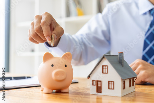 Close up hand of a businessman putting coin in a pink piggy bank, with a small house model on the table, saving or houise mortgage concept photo