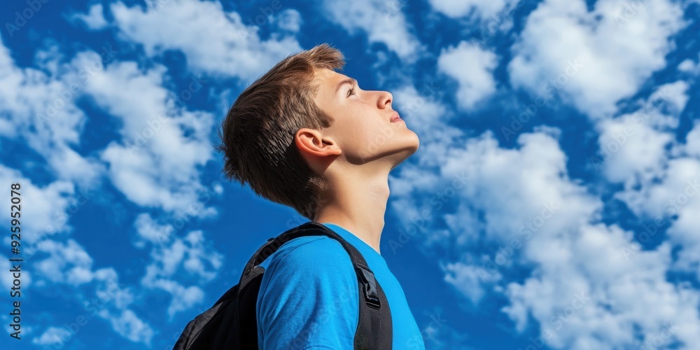 High school boy gazing up at a blue sky filled with clouds High school boy gazing up at a blue sky filled with clouds