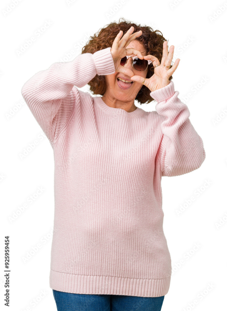 Beautiful middle ager senior woman wearing pink sweater and sunglasses over isolated background Doing heart shape with hand and fingers smiling looking through sign Beautiful middle ager senior woman wearing pink sweater and sunglasses over isolated background Doing heart shape with hand and fingers smiling looking through sign