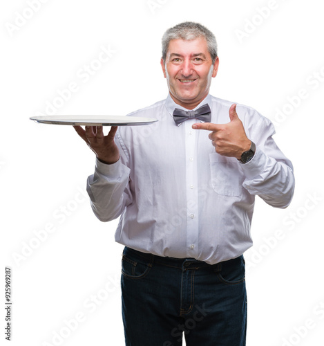 Handsome senior waiter man holding silver tray over isolated background very happy pointing with hand and finger