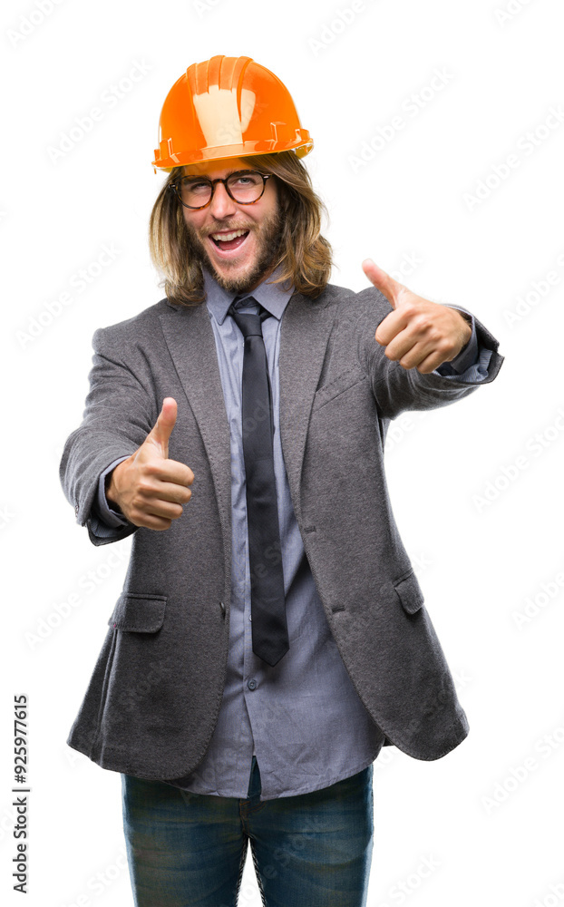 Young handsome architec man with long hair wearing safety helmet over isolated background approving doing positive gesture with hand, thumbs up smiling and happy for success. Looking at the camera Young handsome architec man with long hair wearing safety helmet over isolated background approving doing positive gesture with hand, thumbs up smiling and happy for success. Looking at the camera