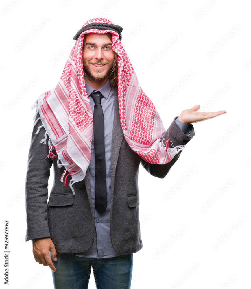 Young handsome arabian man with long hair wearing keffiyeh over isolated background smiling cheerful presenting and pointing with palm of hand looking at the camera.