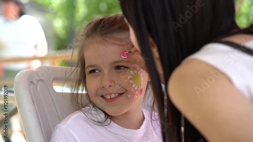 The artist makes a drawing on the girl's face with a face painting. 