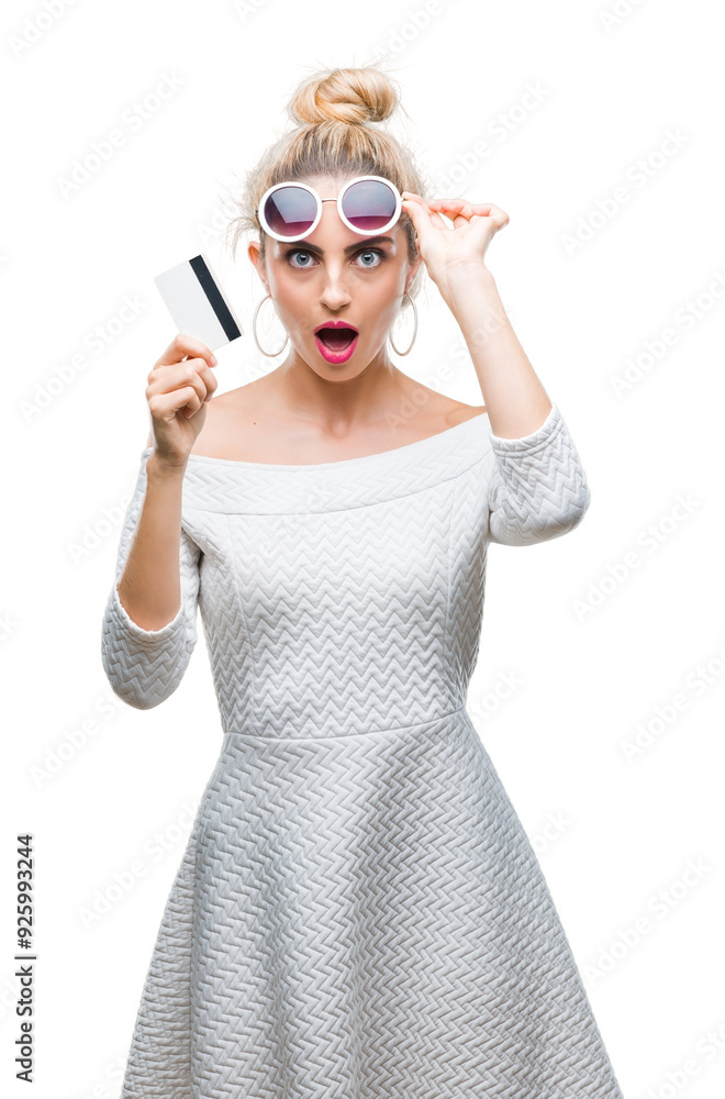 Young beautiful blonde woman holding credit card over isolated background scared in shock with a surprise face, afraid and excited with fear expression Young beautiful blonde woman holding credit card over isolated background scared in shock with a surprise face, afraid and excited with fear expression