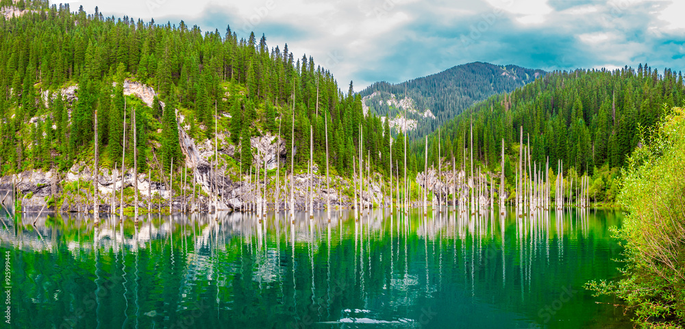 Sunken forest of Lake Kaindy in Kazakhstan. Beautiful mountain natural landscape. A blue lake with tree trunks sticking out of it. Panoramic view of the reserve. Sunken forest of Lake Kaindy in Kazakhstan. Beautiful mountain natural landscape. A blue lake with tree trunks sticking out of it. Panoramic view of the reserve.