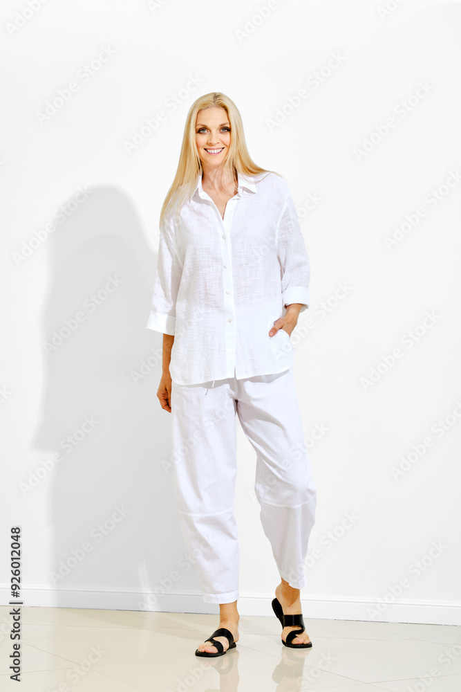 Cheerful woman walking in bright studio in loose white cotton shirt and wide trousers Cheerful woman walking in bright studio in loose white cotton shirt and wide trousers