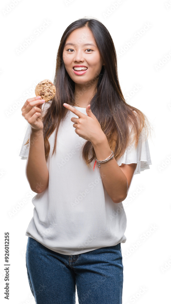 Young asian woman eating chocolate chip cookie over isolated background very happy pointing with hand and finger Young asian woman eating chocolate chip cookie over isolated background very happy pointing with hand and finger