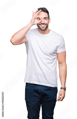 Young man wearing casual white t-shirt over isolated background doing ok gesture with hand smiling, eye looking through fingers with happy face.