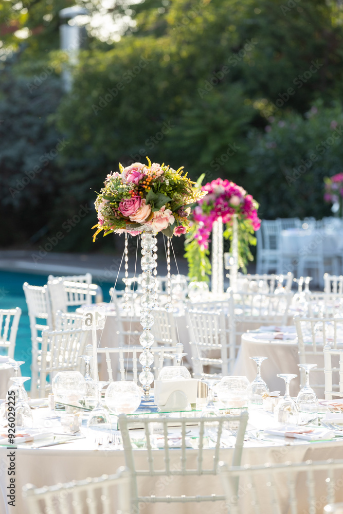 Outdoor wedding reception with round tables, white linens, and tall floral centerpieces