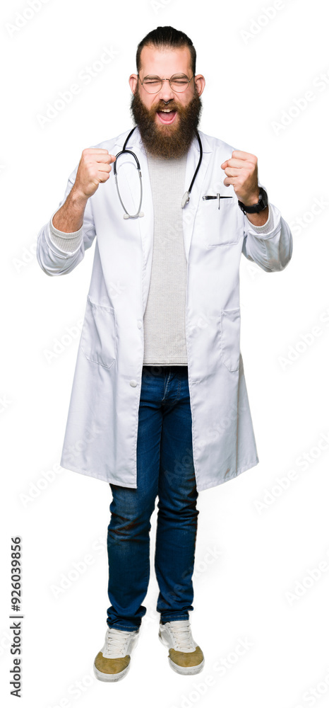 Young blond doctor man with beard wearing medical coat excited for success with arms raised celebrating victory smiling. Winner concept. Young blond doctor man with beard wearing medical coat excited for success with arms raised celebrating victory smiling. Winner concept.