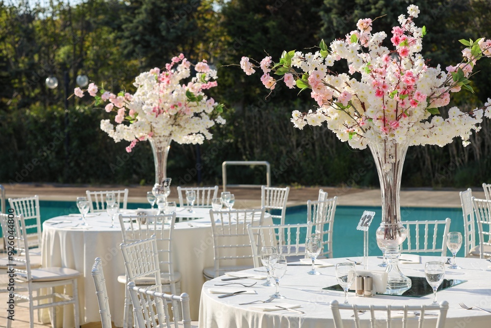A romantic and elegant outdoor wedding reception with round tables and tall floral centerpieces. The flowers are a mix of pink and white, creating a beautiful and dreamy setting