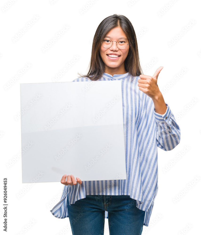Young asian woman over isolated background holding blank banner happy with big smile doing ok sign, thumb up with fingers, excellent sign Young asian woman over isolated background holding blank banner happy with big smile doing ok sign, thumb up with fingers, excellent sign