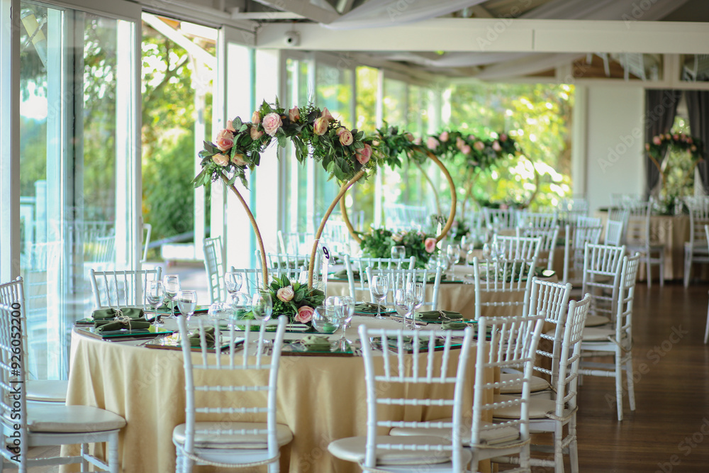 A rustic-chic wedding reception with round tables, white chairs, and floral hoops. The flowers are a mix of pink and green, creating a natural and elegant setting