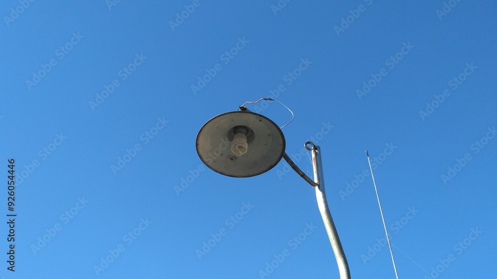 A minimalist photograph of a simple street lamp captured from below against a clear blue sky. The image highlights the contrast between the metal lamp and the vivid sky, evoking a sense of calm A minimalist photograph of a simple street lamp captured from below against a clear blue sky. The image highlights the contrast between the metal lamp and the vivid sky, evoking a sense of calm