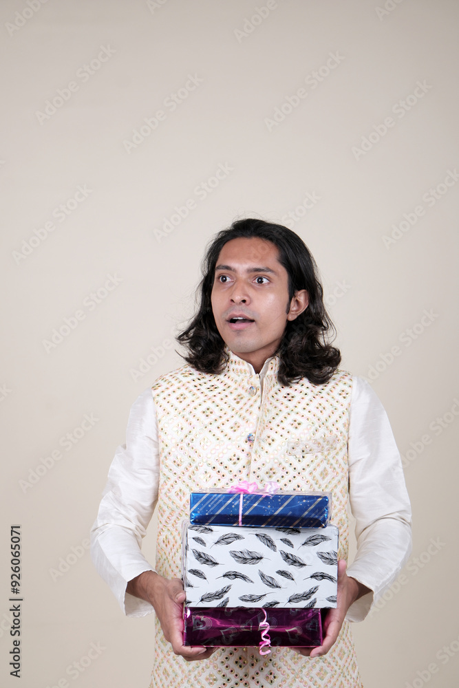 A happy young man in traditional attire, holding gift boxes and looking at the camera against a cream background. A happy young man in traditional attire, holding gift boxes and looking at the camera against a cream background.