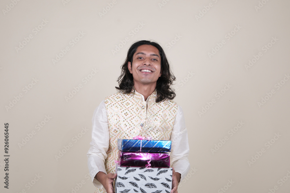 A happy young man in traditional attire, holding gift boxes and looking at the camera against a cream background. A happy young man in traditional attire, holding gift boxes and looking at the camera against a cream background.