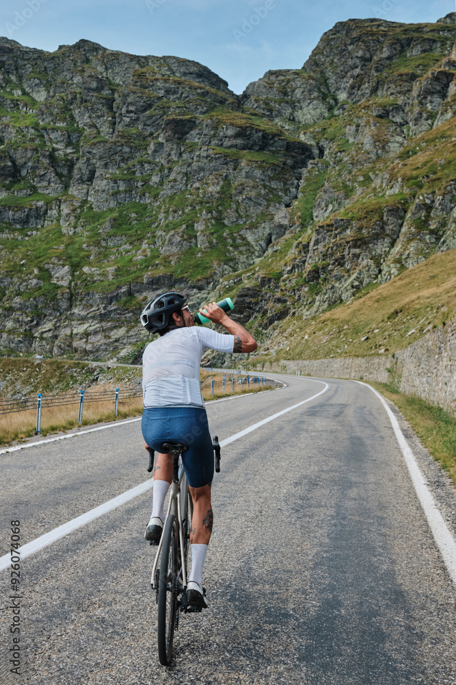 Fototapeta premium Man cyclist in cycling kit and a helmet is drinking water from a sports bottle during training.