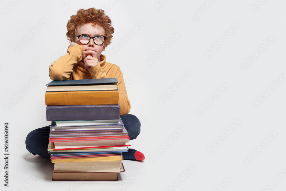 Thinking child schoolboy with stack of books against white studio wall banner background with copy space Thinking child schoolboy with stack of books against white studio wall banner background with copy space