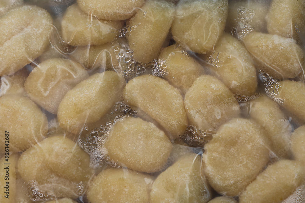 Fototapeta premium Vacuum-sealed pack of gnocchi, showing fresh, soft, pillowy dumplings. The clear packaging highlights the golden, potato-based pasta, ready for cooking.