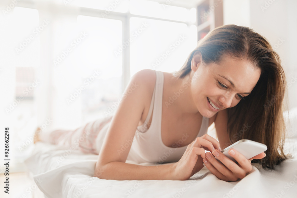 Smiling young woman using smartphone in bed at home Smiling young woman using smartphone in bed at home