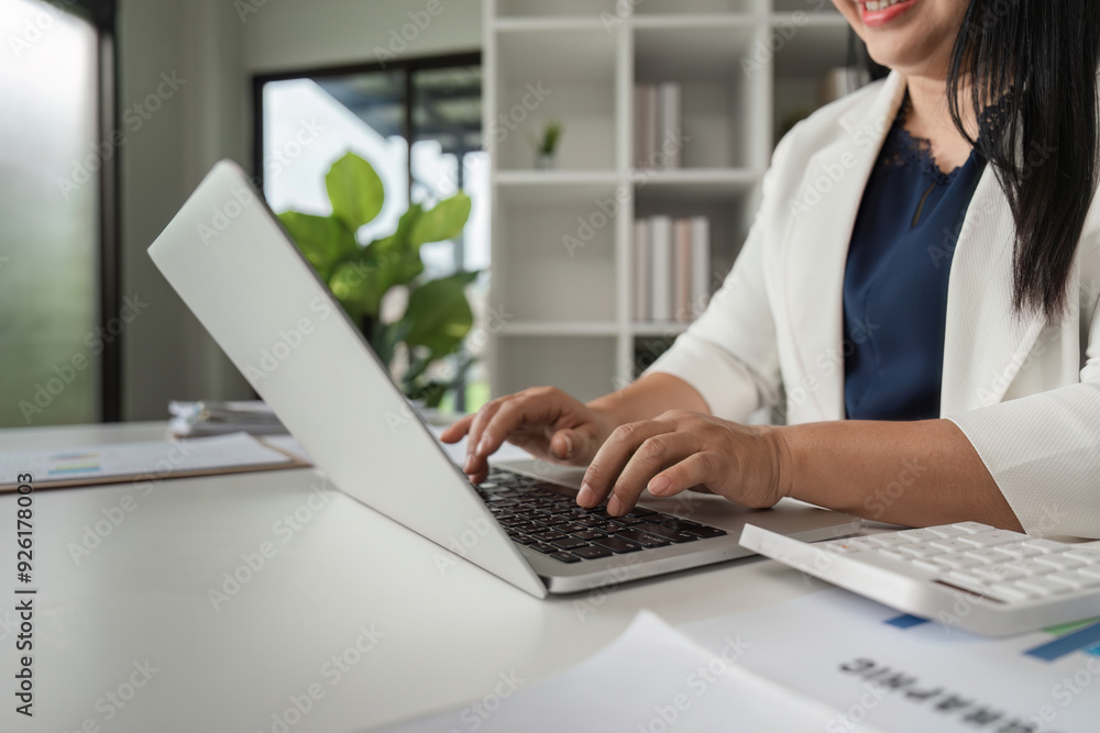 Middle-aged Business Woman Doing Paperwork and Working on Laptop in Modern Office Setting Middle-aged Business Woman Doing Paperwork and Working on Laptop in Modern Office Setting