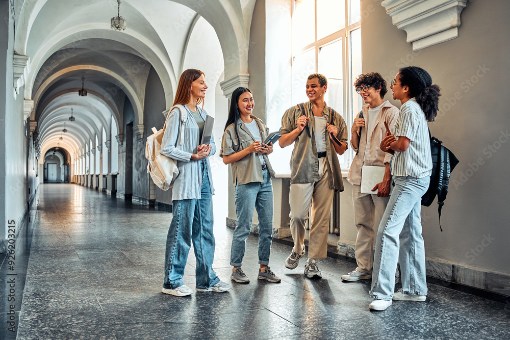 Obraz premium College students stand and talk in the university building. Multiethnic young people stand near classes, diverse college friends spending time indoors after lessons.