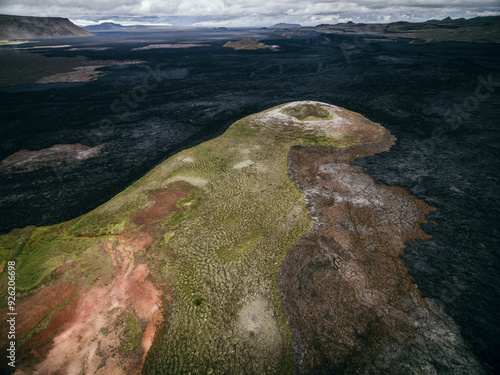 Verlassene Vulkanlandschaft mit einem erloschenen Krater, umgeben von schwarzem, erkaltetem Lavagestein und farbenfrohem Moos in einer abgelegenen Region photo