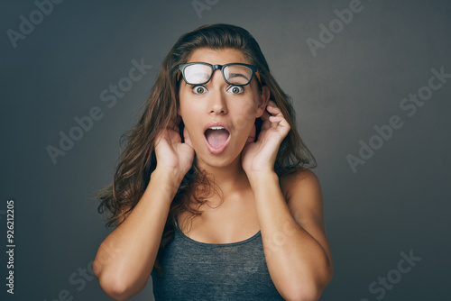 Woman, portrait and surprise with glasses in shock for news, alert or notification on a gray studio background. Face of young female person or model expression in disbelief or wow for rumor or gossip photo