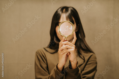 Curiosity Unmasked: A young woman peers through a magnifying glass, her gaze both playful and inquisitive.  photo