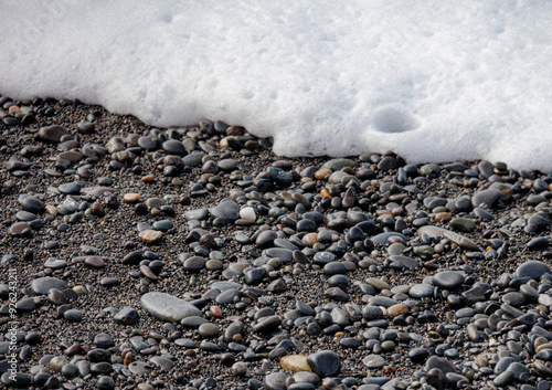 Wave of sea foam hitting pebbles on the beach