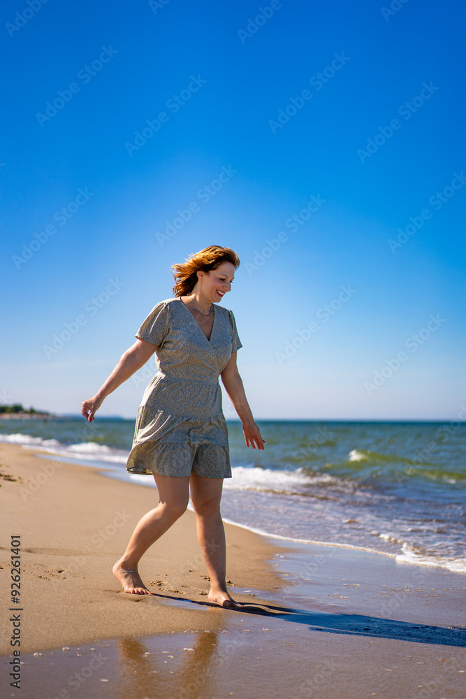 Summer holidays. Young beautiful woman wearing light dress walking on sandy beach by sea shore on sunny day. Beauty, joy of life and youth. Summer holidays. Young beautiful woman wearing light dress walking on sandy beach by sea shore on sunny day. Beauty, joy of life and youth.