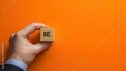 A hand holding a wooden block with the letters BE on it