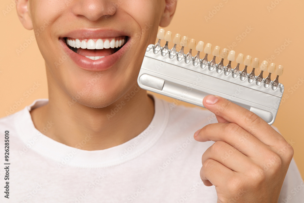 Happy young man with teeth color samples on beige background, closeup. Dental veneers Happy young man with teeth color samples on beige background, closeup. Dental veneers