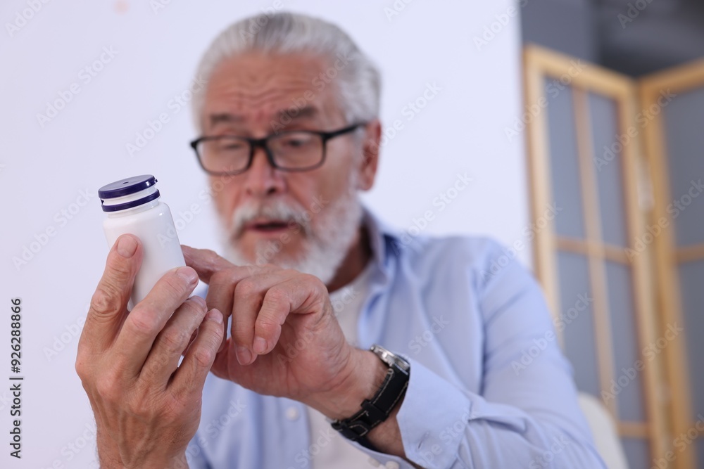 Senior man with bottle of pills at home, selective focus Senior man with bottle of pills at home, selective focus