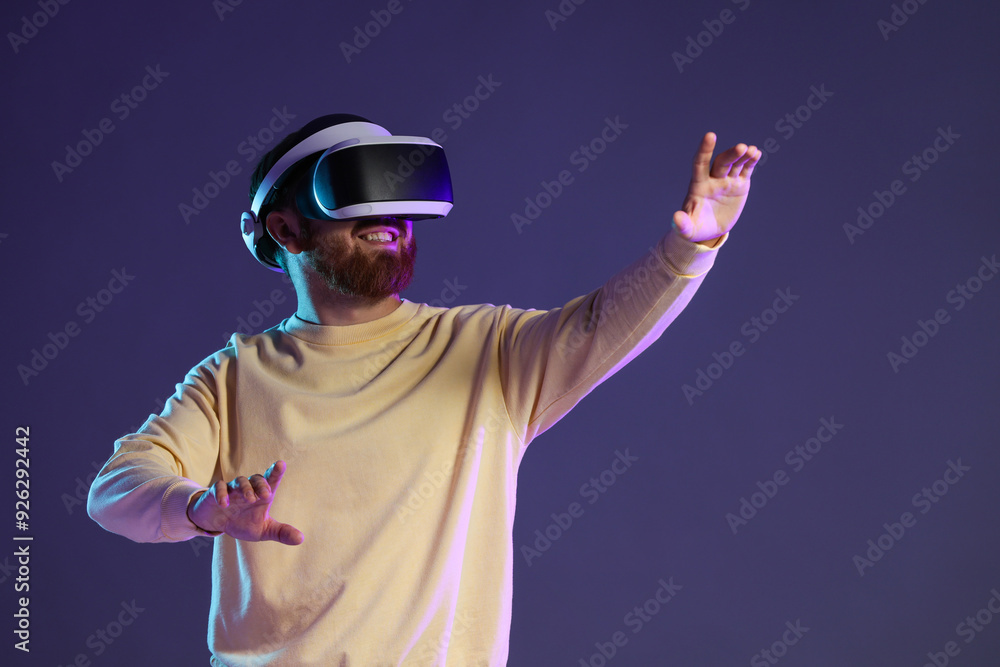 Smiling man using virtual reality headset on dark purple background. Space for text Smiling man using virtual reality headset on dark purple background. Space for text