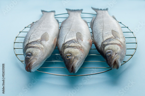 Fresh raw sea bass fish on the grill on a blue background. Proper nutrition, Mediterranean diet.