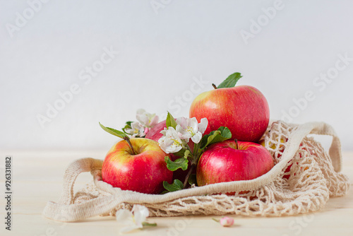 Still life, composition with sweet ripe fresh apples, red organic fruits with flowers of apple tree in organic knitted rag bag, eco friendly. Harvesting