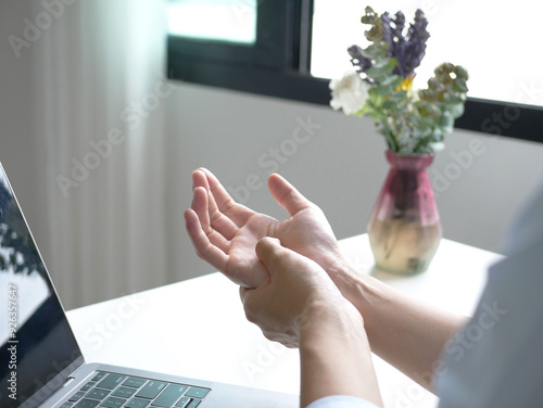 Young business woman massages her palm in pain It is caused by working on a laptop keyboard for long periods of time, resulting in wrist pain and numbness in the wrist. While working at the office photo