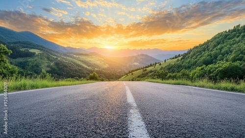Empty highway stretches into distance, surrounded by lush green mountains. Vibrant sunset paints sky in golden hues. Perfect blend of nature and infrastructure, ideal for road trip enthusiasts.