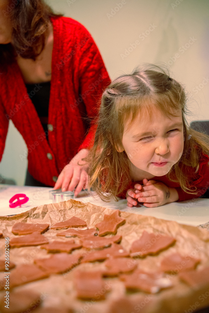 A young mother and her beautiful daughter are making Christmas cookies. The mother and daughter, wearing red sweaters, are making New Year's style cookies, cutting out different shapes with molds A young mother and her beautiful daughter are making Christmas cookies. The mother and daughter, wearing red sweaters, are making New Year's style cookies, cutting out different shapes with molds