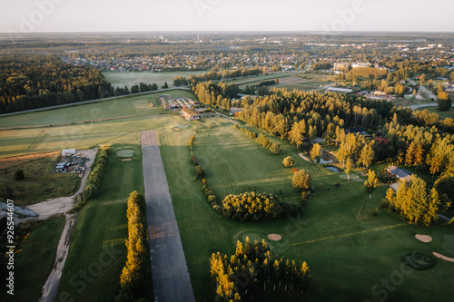 Valmiera, Latvia - August 15, 2024 - Aerial view of a golf course with fairways, greens, bunkers, and surrounding trees, adjacent to a small town at sunrise. Copy space photo