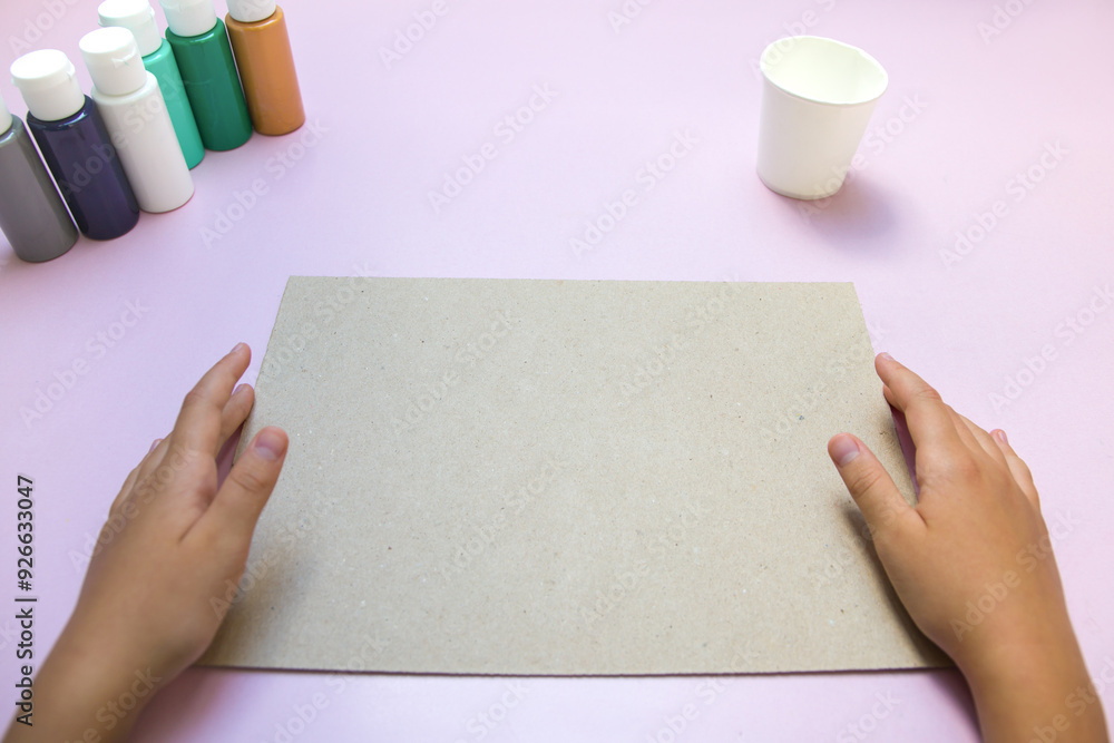 Obraz premium Paints, paper cup and sheet of paper holding hands on pink background. Acrylic painting.